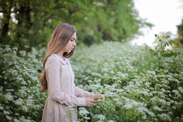 Dreamy relaxed and happy teenager girl taking photo with old camera, walk in the blooming meadow surrounded by white flowers of ground elder in the magic light of sunset in vintage linen dress