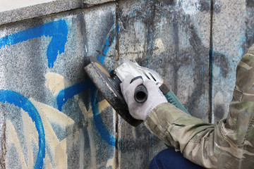 Removal of graffiti on a concrete wall of an underground passage with the help of a angle grinder. - obrazy, fototapety, plakaty