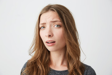 Portrait of young beautiful girl looking at camera suspiciously with opened mouth over white background.