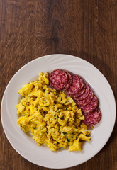 scrambled eggs with salami in a plate on wooden table with copy space. top view