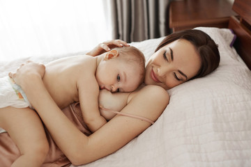 Obraz na płótnie Canvas Young beautiful happy mom breastfeeding hugging her baby lying on bed at home.