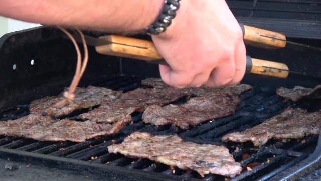 Man's hands cooking meat on grill