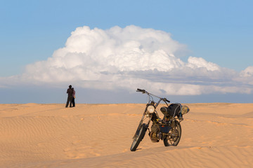 Men and woman with motorcycle in the desert against a cloudy sky background