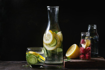 Citrus cucumber berries blueberry and raspberry sassy sassi water for detox in glass bottles on dark black background. Clean eating, healthy lifestyle concept, sunlight