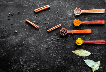 spices in wooden spoons on dark background top view