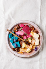 Variety of colorful holland cheese traditional soft, old, pink basil, blue lavender served with pecan nuts, honey, lavender flowers on terracotta plate over white linen background. Flat lay
