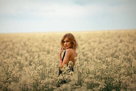 Young woman in black dress among flowering meadow.