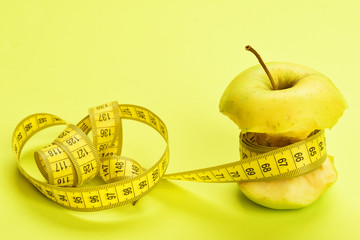 Apple wrapped around by measure tape on bright yellow background