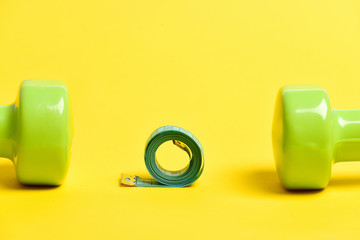 Roll of cyan measuring tape between pair of green dumbbells