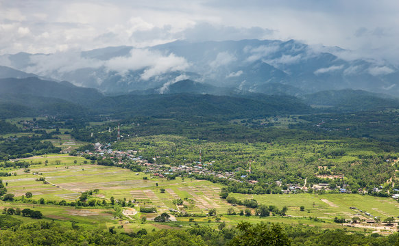 Panorama view of green land with sunlight and mountain covered by cloud and fog in countryside of Thailand on rainy season.
