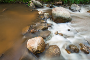Scenery of brown watercourse with flowing water and white wave on rock river.