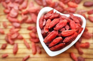 Dried goji berries in heart-shaped bowl, selective focus