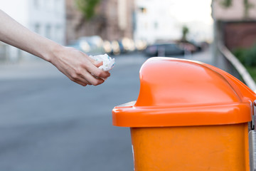 Throwing waste into a an orange trash can in the street