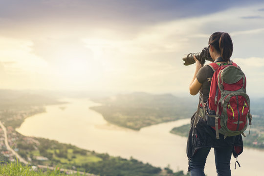 Woman photographer taking photos of beautiful sunset behind the city and river on the mountain.