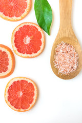 Ayurveda face skin scrub ingredients, pink Himalayan salt in wooden spoon, sliced grapefruit, green leaf on white background, beauty, health, wellness