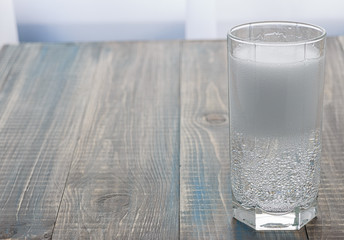 A glass with transparent sparkling water is on the wooden table on the right. There is an empty place on the left