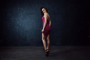 Fototapeta na wymiar Glamorous stylish fashion model in a red dress posing stands on dark background. Fall fashion. Vogue Style.