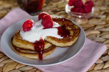Three pancakes served with sour cream, jam and raspberries