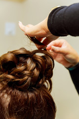 Woman hairdresser making hairstyle using curling iron for long hair of young female