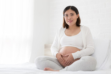 Happy pregnant woman sitting on bed at home, Pregnancy concept