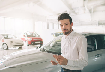 friendly vehicle salesman presenting new cars at showroom. Photo of young male consultant showing new car in auto show. Concept for car rental