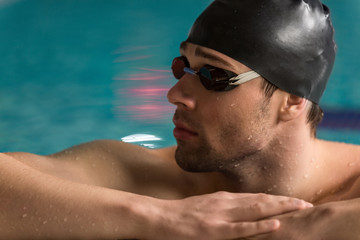 Male swimmer wearing goggles and swimming cap resting