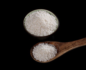 White rice in a bowl and wooden spoon isolated on black background