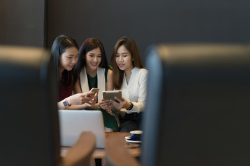 Three beautiful Asian girls using smartphone and laptop, chatting on sofa at cafe, modern lifestyle with gadget technology or working woman on casual business meeting outside office concept.