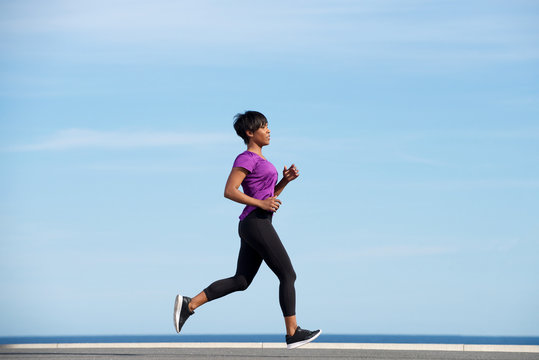 Full Body Side Fit Young African Woman Running Outdoors Against Blue Sky