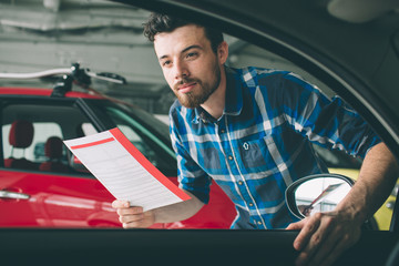 Perfect lines. The young dark-haired bearded man examining car at the dealership and making his...