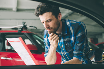 Perfect lines. The young dark-haired bearded man examining car at the dealership and making his...