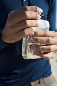 Close up view on man graceful hands opening metal flask with clean fresh water in desert. Vertical shot.