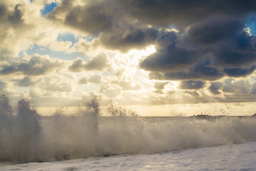 Beautiful sunset among the unimaginable clouds with glimpses of rays on the sea with waves