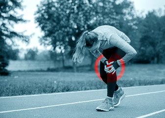Athletic woman on running track touching hurt leg with knee injury