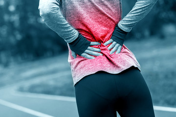 Athletic woman on running track touching hurt back with painful injury