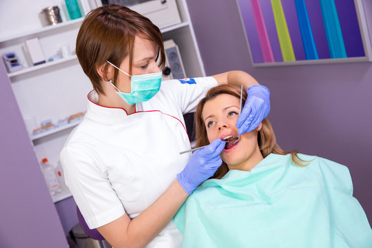Female dentist in mask checking with a dental probe and mirror female patient in  dental clinic office - people, medicine, stomatology and health care concept.
