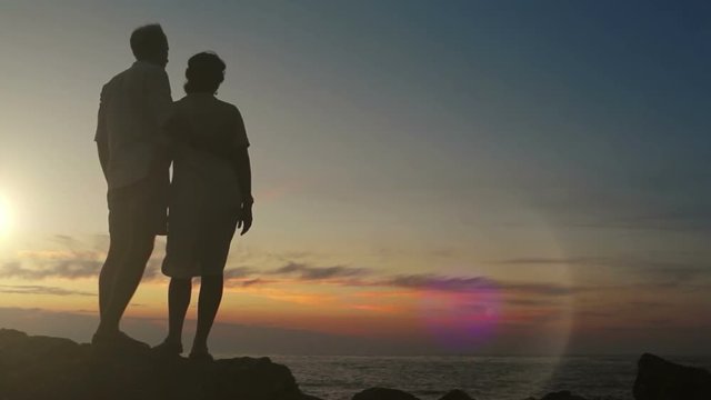 Couple stands on the rock at sunset holding hands