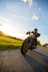 Obraz premium Ciemny motocyklista jadący na motocyklu dużej mocy o zachodzie słońca