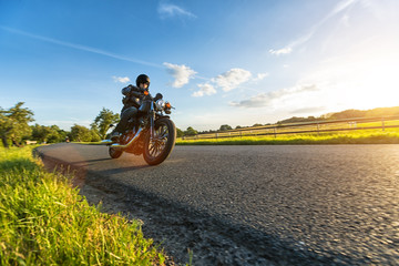 Obraz premium Ciemny motocyklista jadący na motocyklu dużej mocy o zachodzie słońca