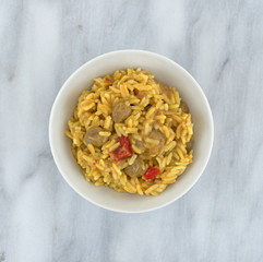 Pilau rice mixed with Korma curry sauce in a white bowl atop a gray marble table top.