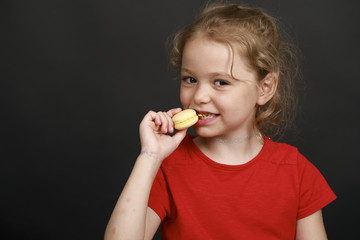 Little blonde girl with freckles opened her mouth and wants to eat macaron yellow cake
