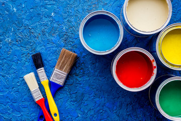 Colorful paints and brushes on blue wooden desk background top view