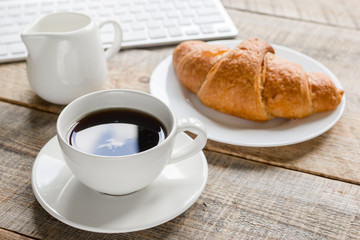 coffee and croissant for breakfast of businessman wooden office desk background