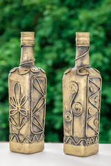 Gold bottle decorated with pattern of flowers on a natural green background, made by hands, hobby