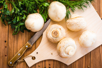 whole fresh champignons on cutting board, parsley and knife on wooden table. Top view