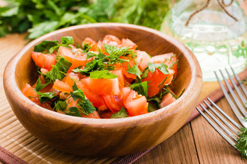 Close-up of salad made of tomatoes and fresh herbs, vegetable oil and fork on wooden table