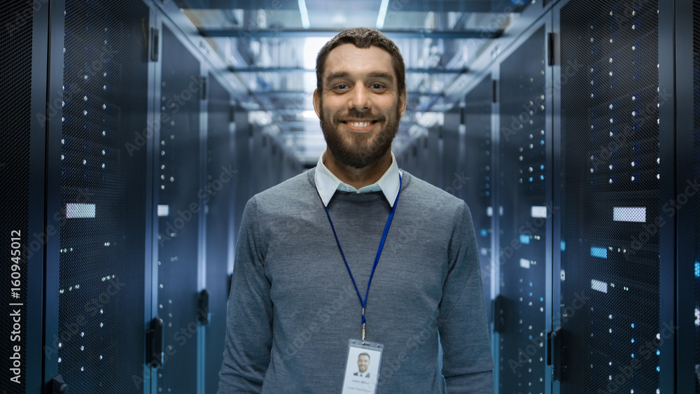Poster portrait of a curios, positive and smiling it engineer standing in the middle of a large data center