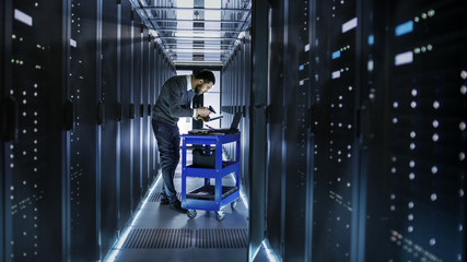 IT Engineer Works on a Laptop and Scans Hard Drives That are Lying on a Crash Cart. He Works in Data Center.