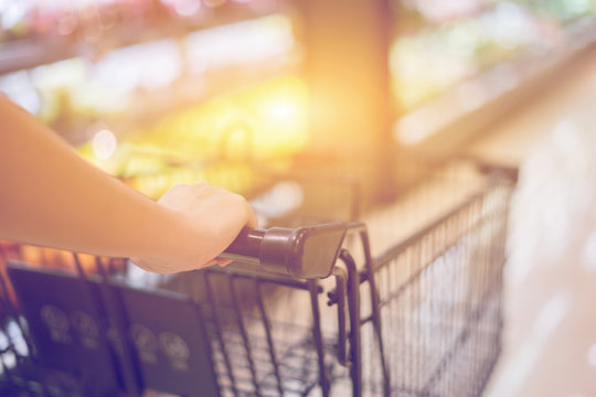 Female Hand Close Up With Shopping Cart in a Supermarket Walking Trough the Aisle,trolley in department store bokeh background,vintage color,copy space