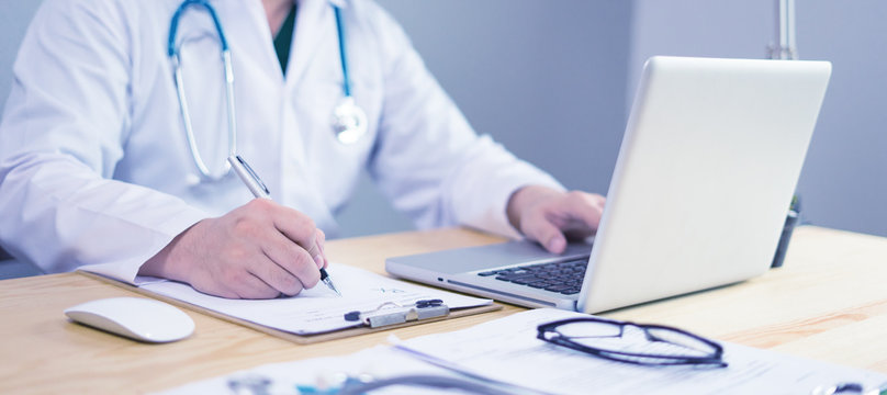 Doctor working in hospital writing a prescription, Healthcare and medical concept,test results in background,Stethoscope with clipboard and Laptop on desk,vintage color,selective focus